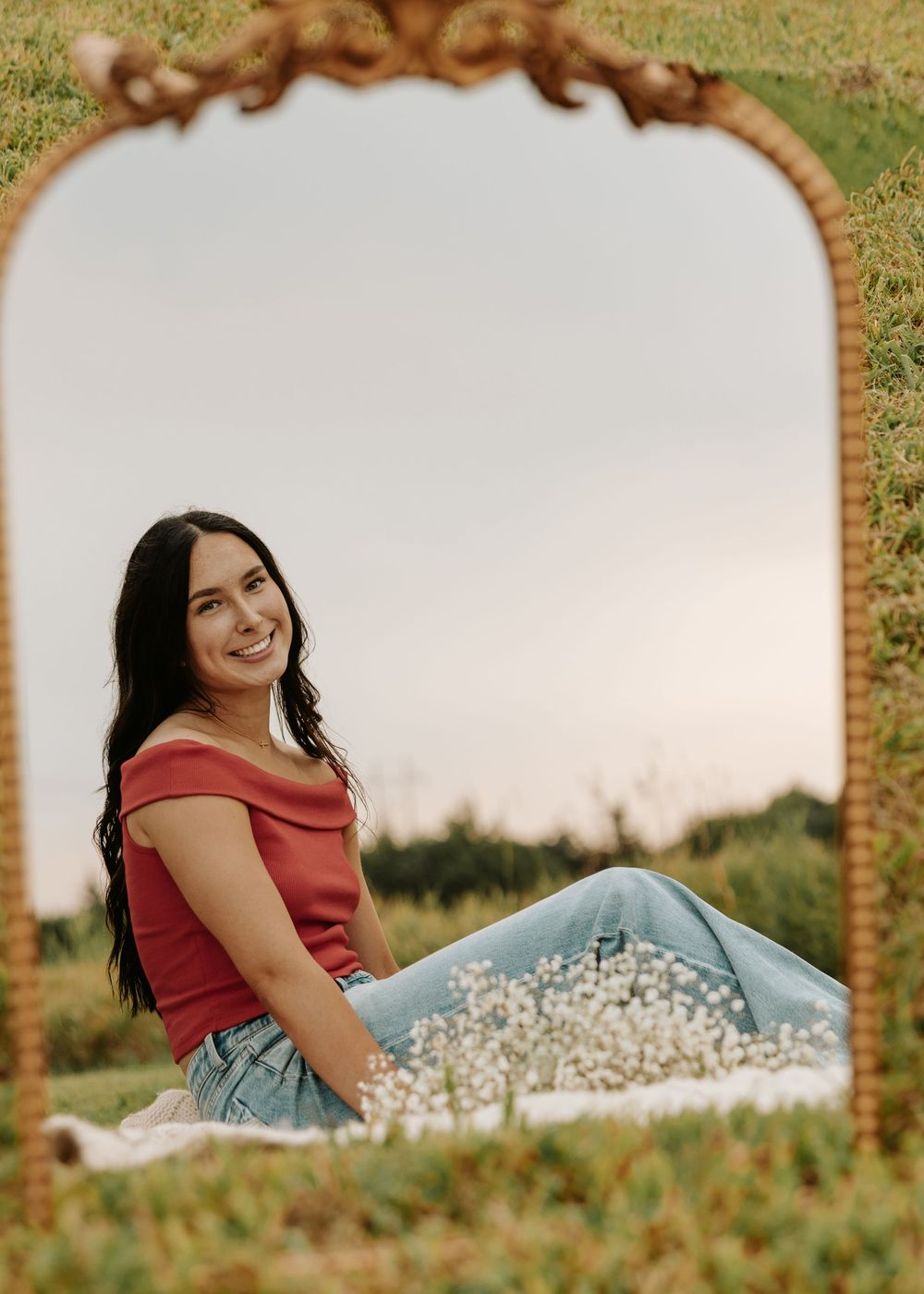 A woman in a red dress lies in a grassy meadow on a sunny day creating a dreamy outdoor portrait series.