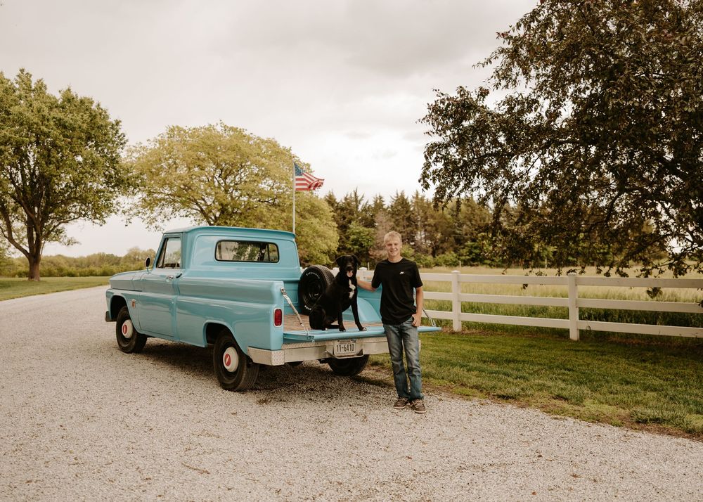 A vintage light blue station wagon parked in a gravel lot during a fall afternoon gathering.