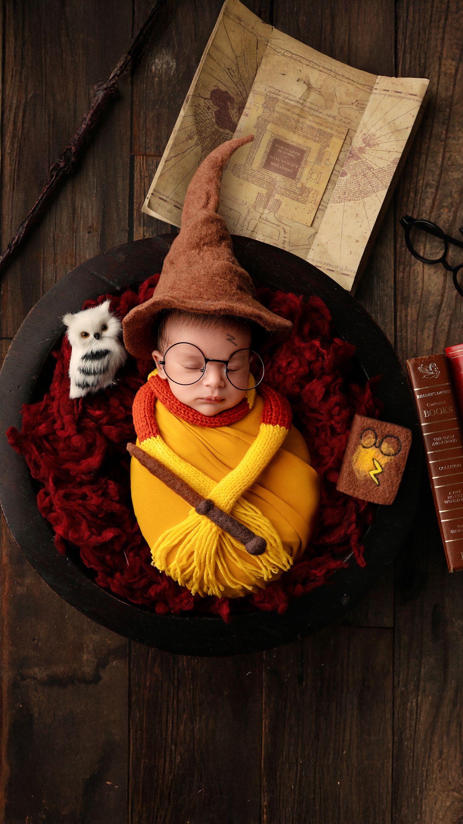 Sleepy newborn baby wrapped in yellow and with Harry Potter props and accessories during professional photoshoot in Hayes, West London