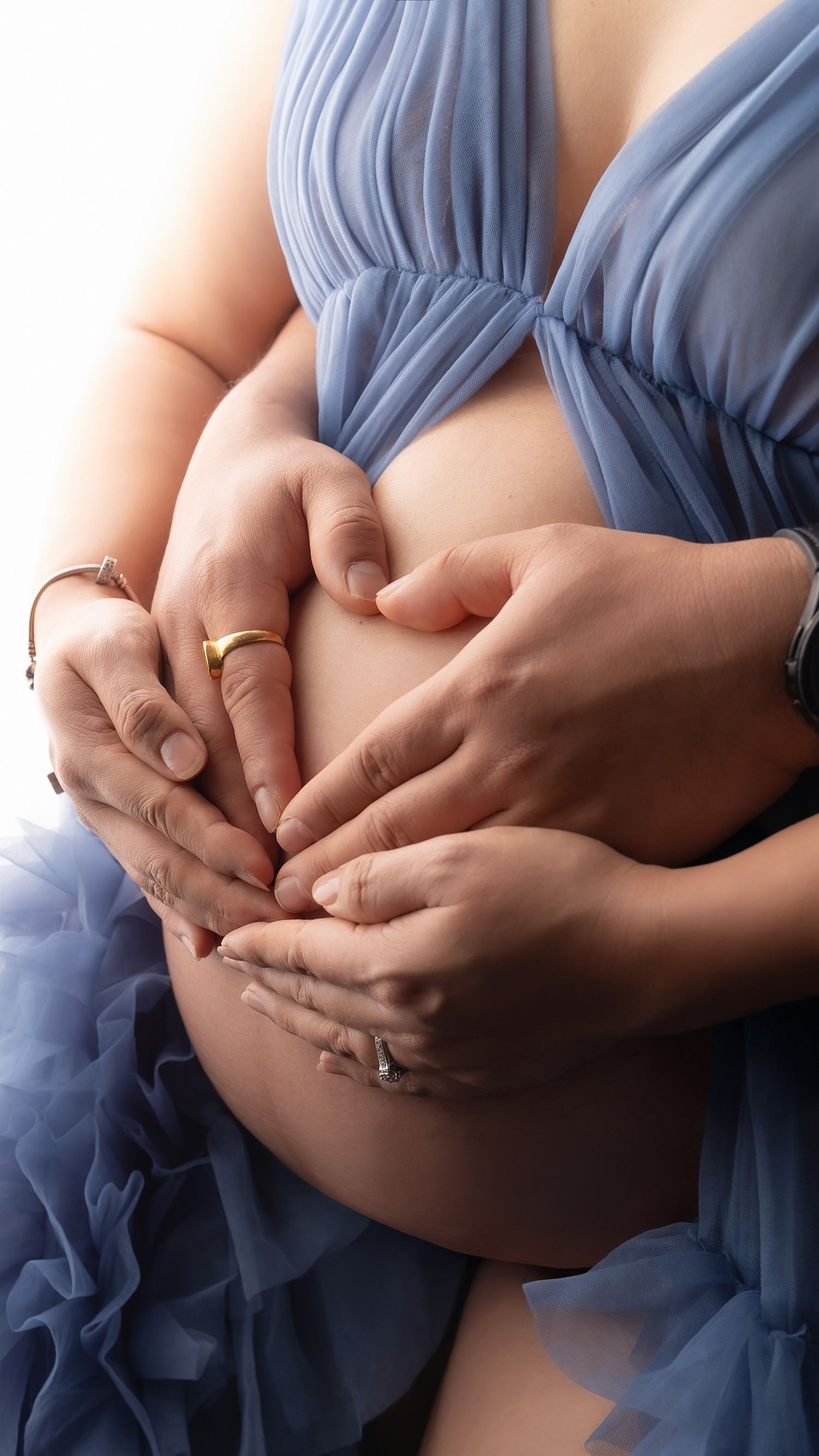 Elegant indoor maternity portrait of expectant mother and her partner holding the bump at 32 weeks pregnant in London studio