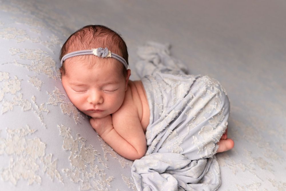 Sleeping newborn baby wrapped in soft gray fabric in artistic collage style photography.