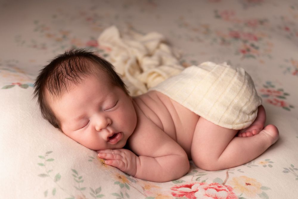 Sleeping newborn on floral patterned fabric with cream wrap.