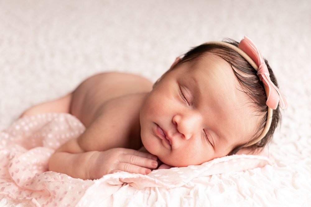 A sleeping newborn baby lies peacefully on soft pink blankets in a studio photography setting.