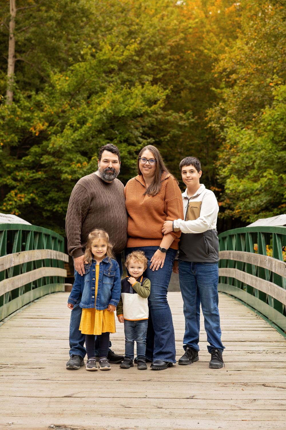 A group stands together on a wooden footbridge surrounded by autumn foliage in a park setting.