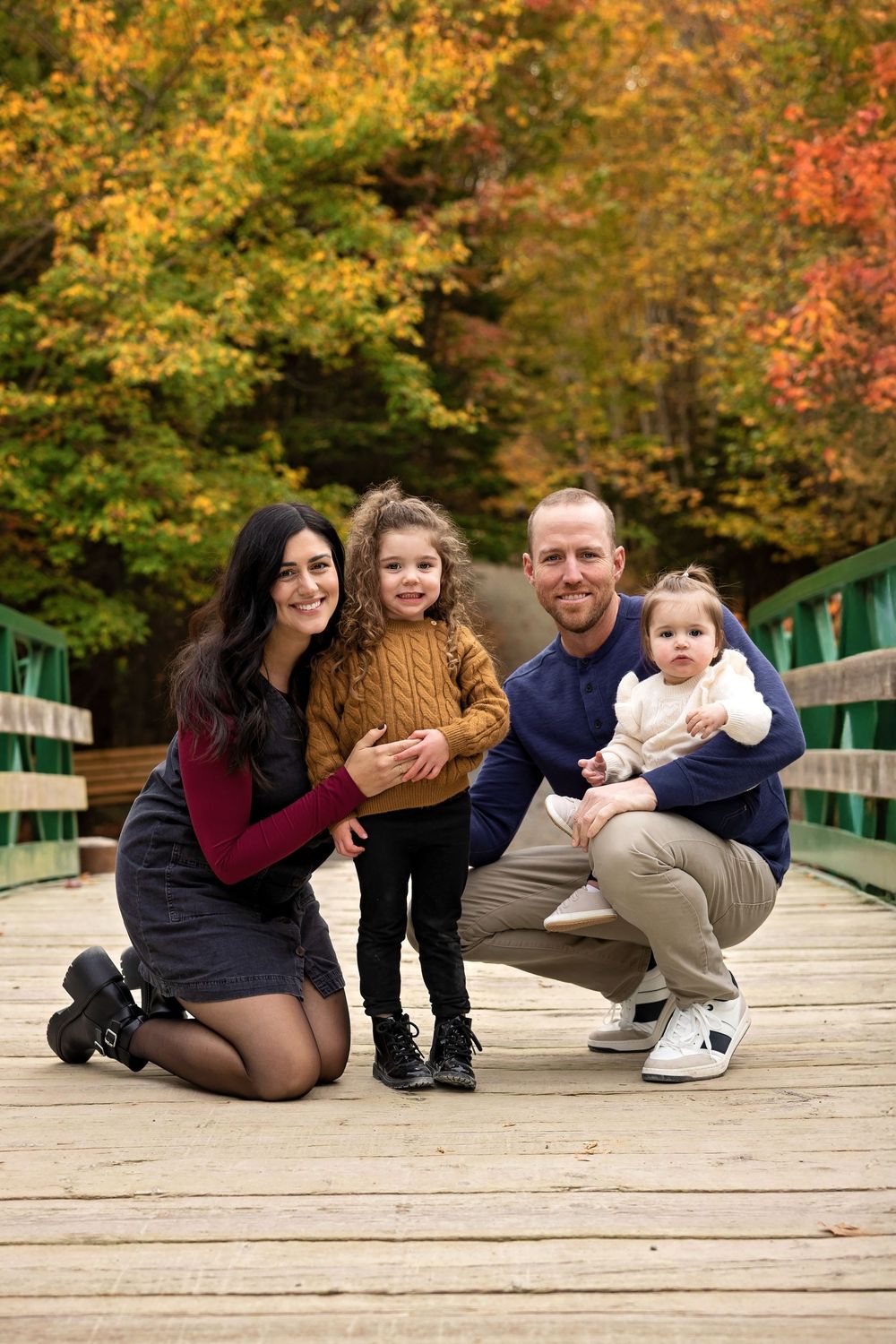 A group sits together on a wooden bridge walkway surrounded by vibrant autumn foliage in the background.