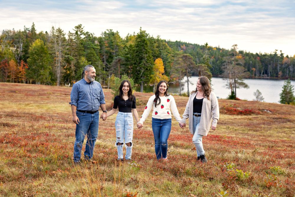 A group walks together on a hillside overlooking a lake during autumn with fall foliage and evergreen trees in view.