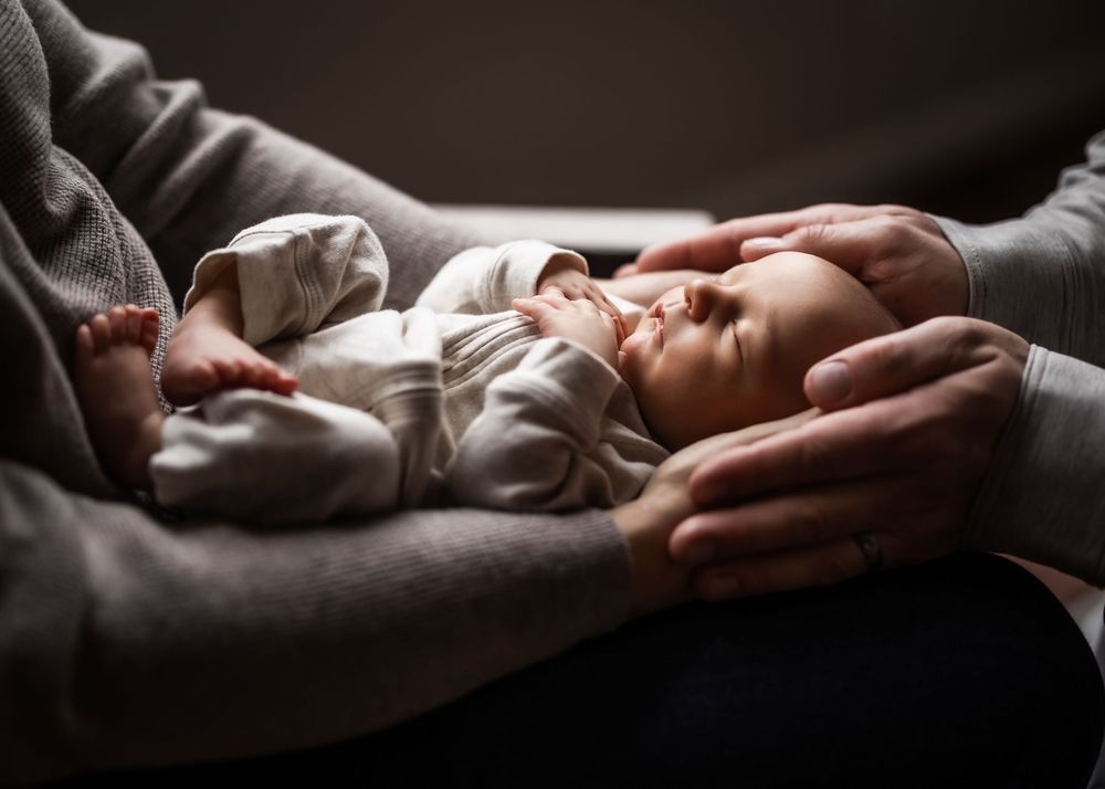 Newborn baby sleeping peacefully in parent's arms, cradled gently with a loving hand on its head.