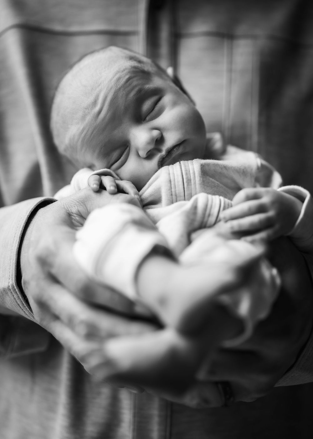 Black and white photo of a sleeping newborn baby cradled gently in adult hands.