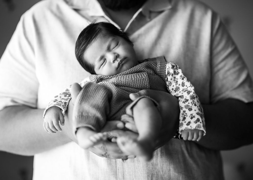 A sleeping infant rests peacefully in black and white, nestled in soft fabric with a patterned sleeve.