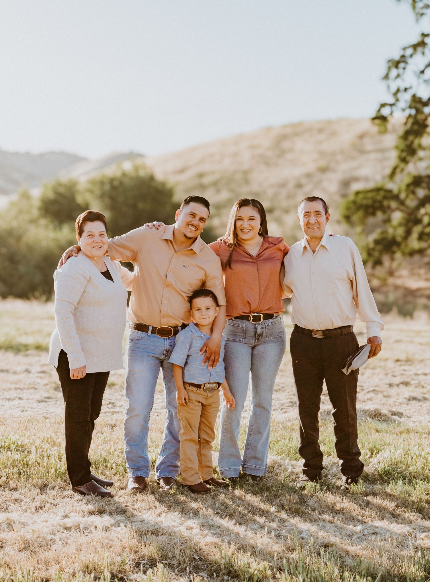 A family of five poses together outdoors against a desert mountain backdrop.
