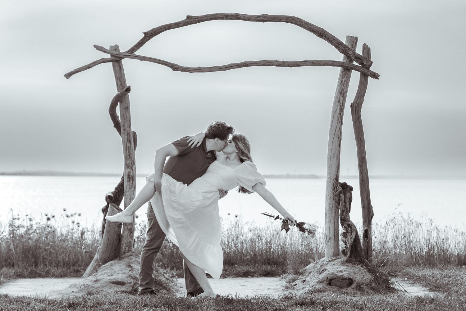 Engagement photography: a man dips and kisses a woman in front of a wooden arch with the Delaware River in the background