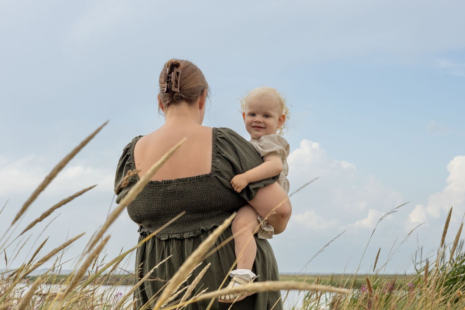 Parent holds child while standing among tall grass in natural setting.