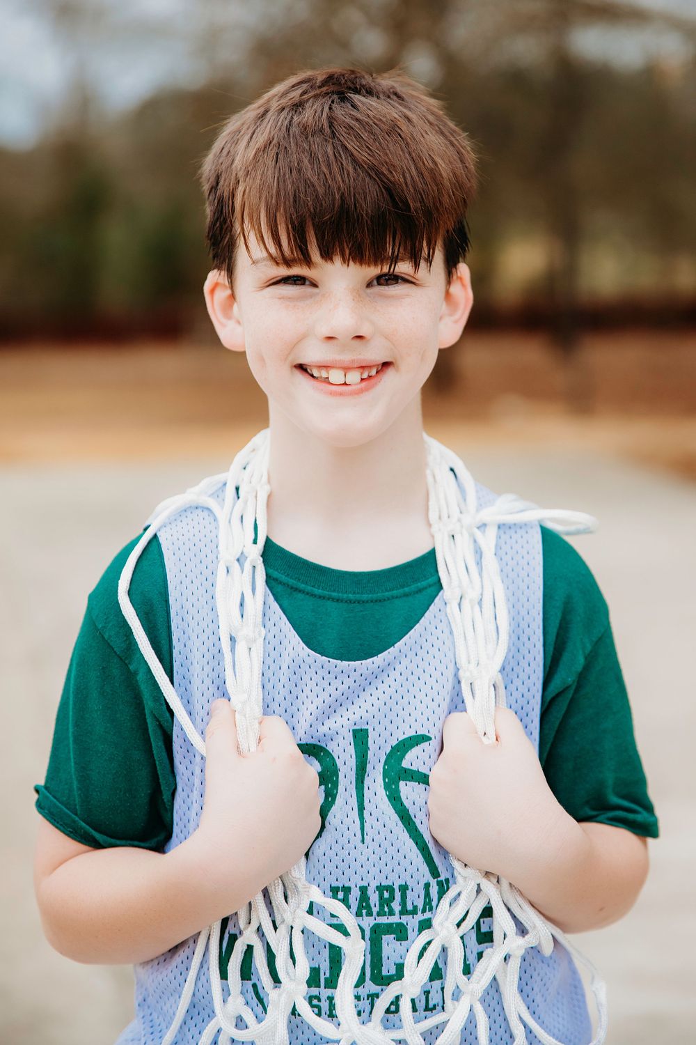 Youth athlete smiles while holding basketball net in outdoor court setting.