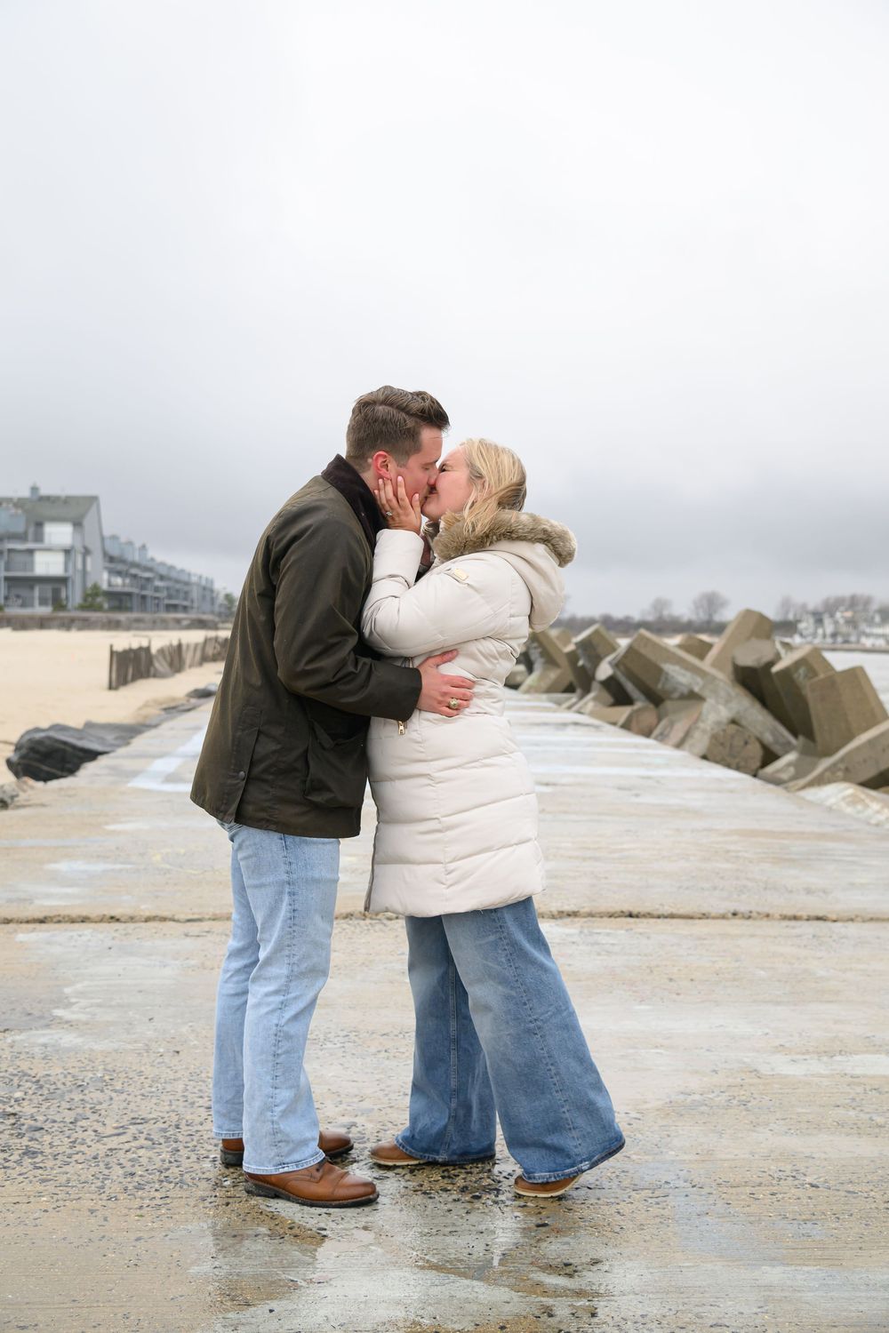 A couple embraces on a cloudy day at a beach with concrete barriers.