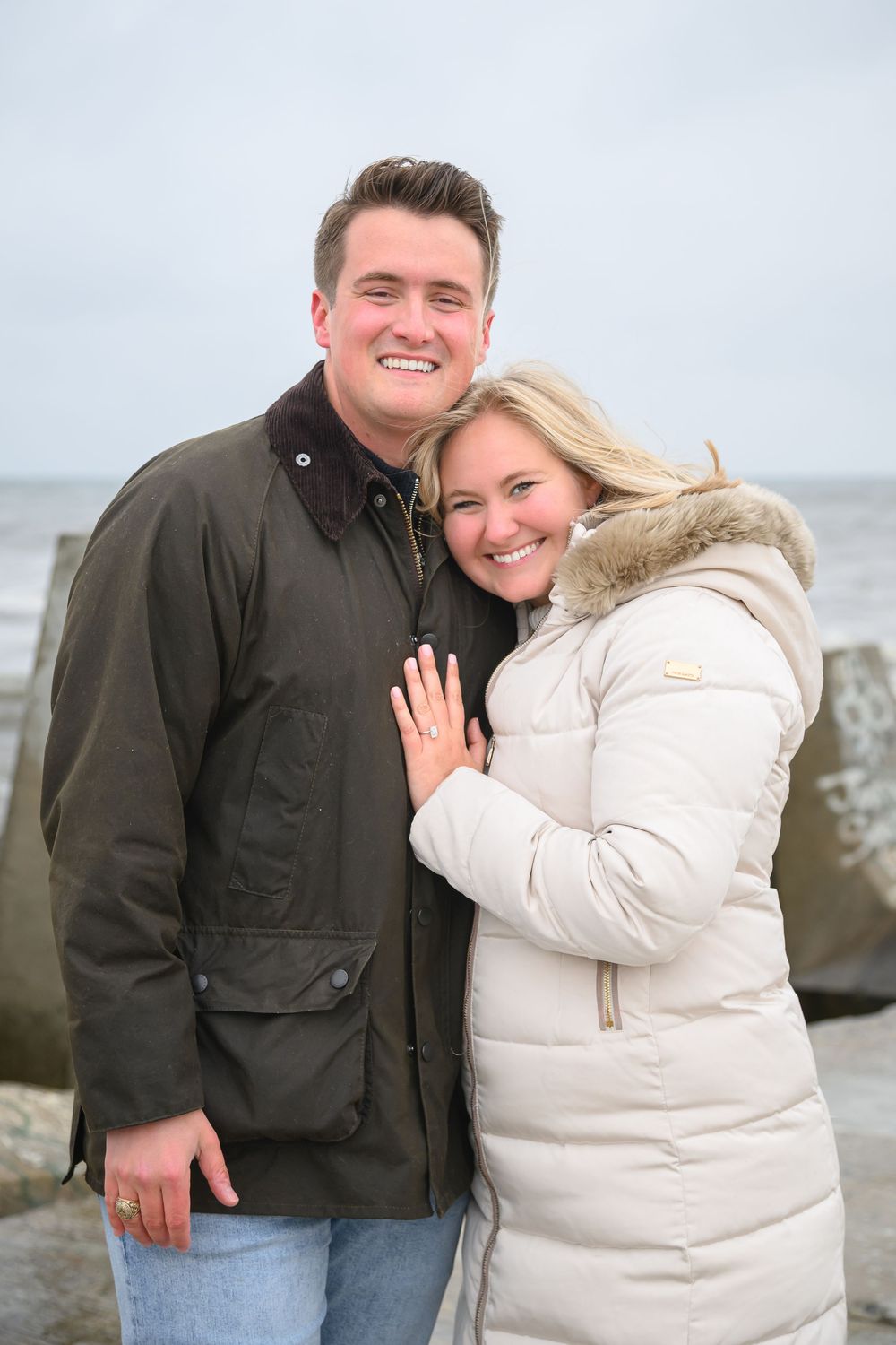 A couple shows off their engagement ring at a coastal location.