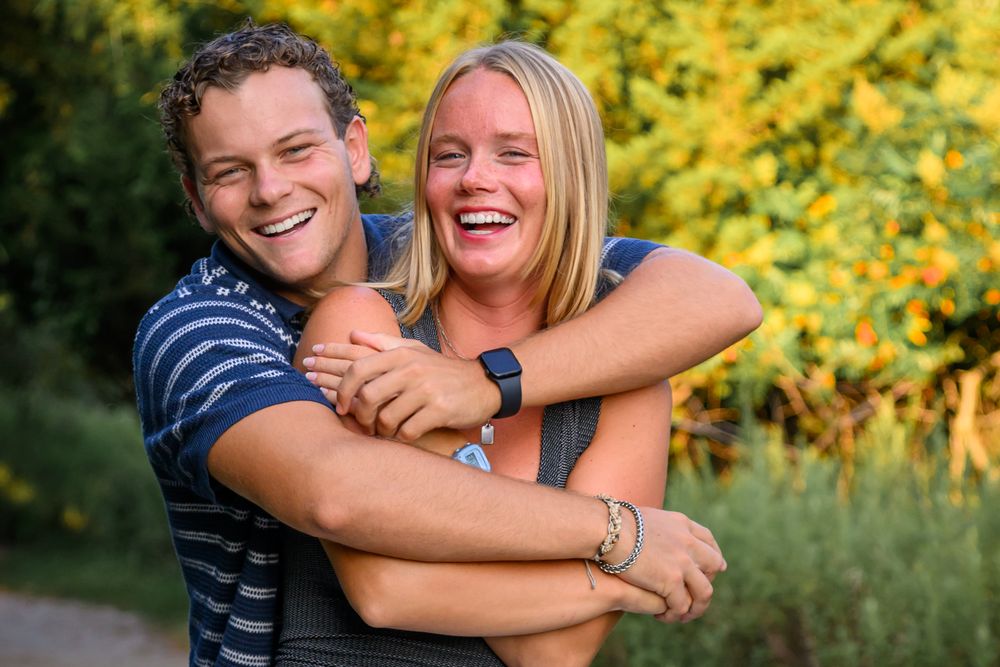 Two people share a joyful embrace while laughing together outdoors with yellow foliage in the background.