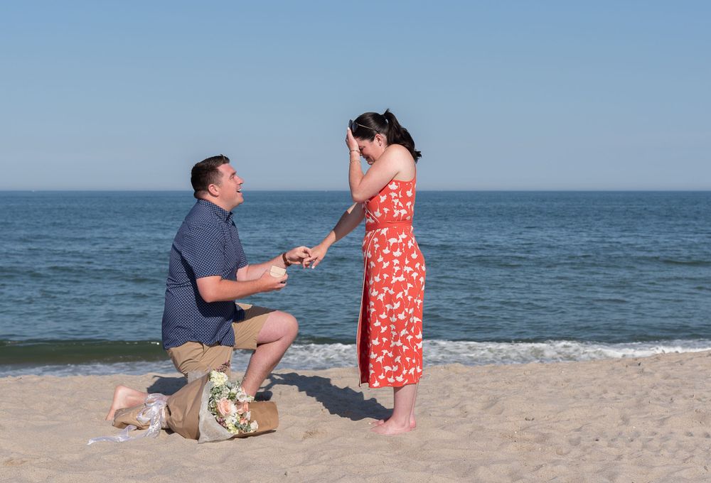 A couple shares a special moment during a beach proposal with ocean waves in the background.