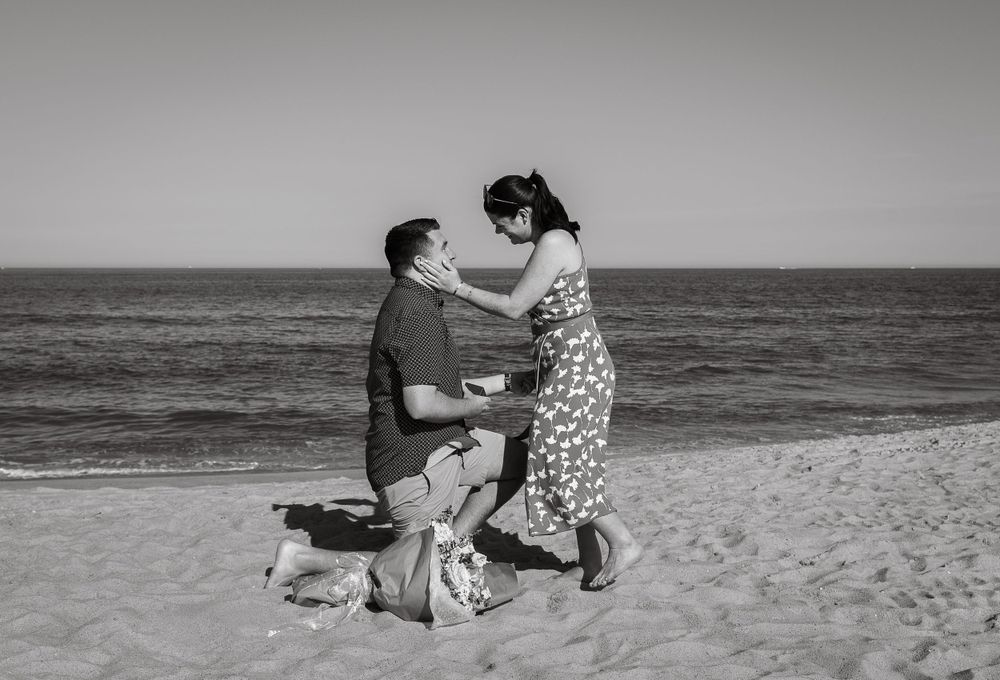A romantic beach proposal scene with a couple on the sand at sunset.