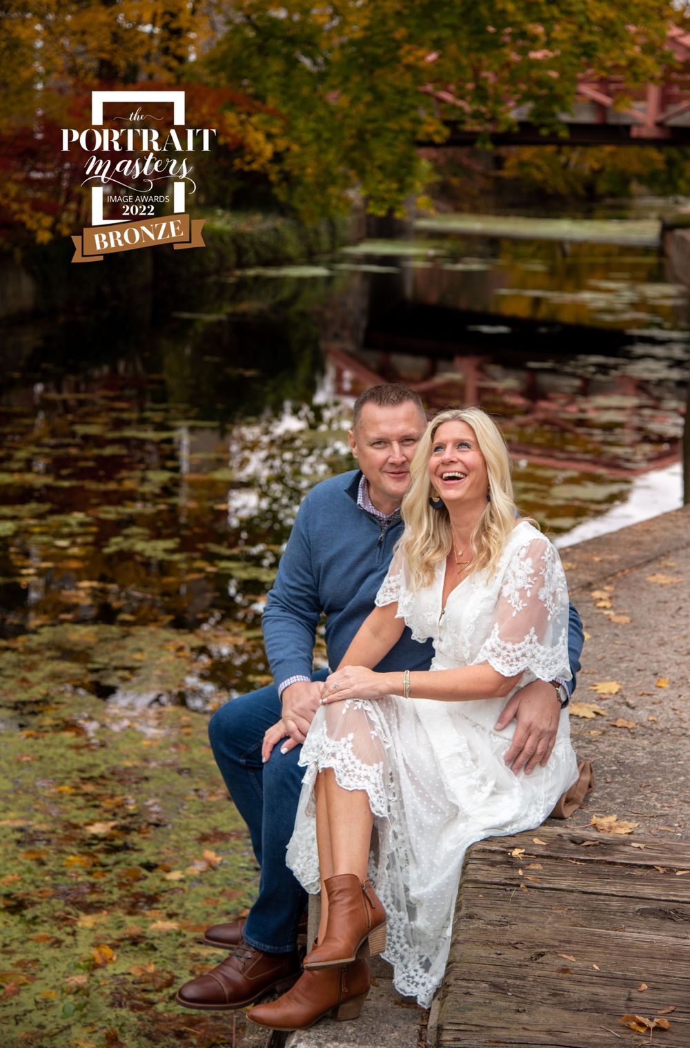 Romantic autumn engagement photo on wooden dock surrounded by fall foliage.