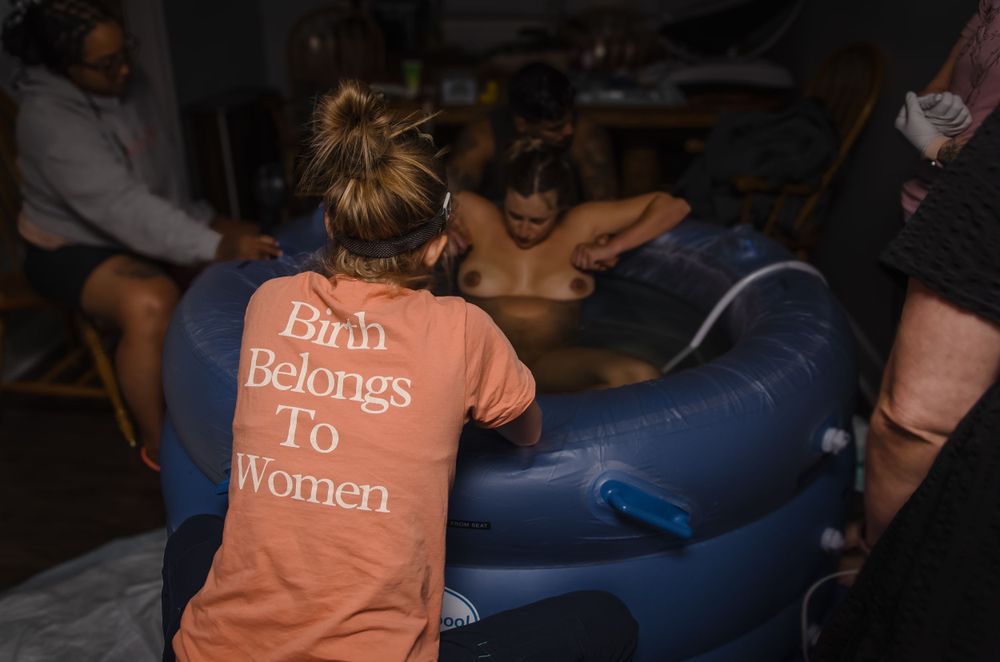 Birth attendant wearing shirt with empowering message assists during labor.