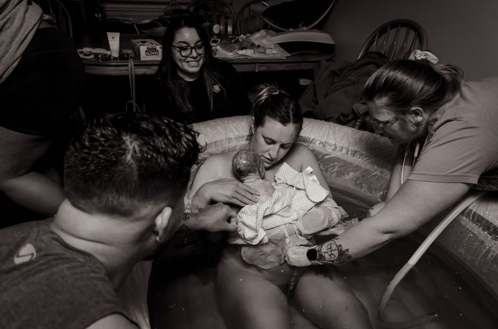 Birth team gathers around newly delivered baby in birthing pool.