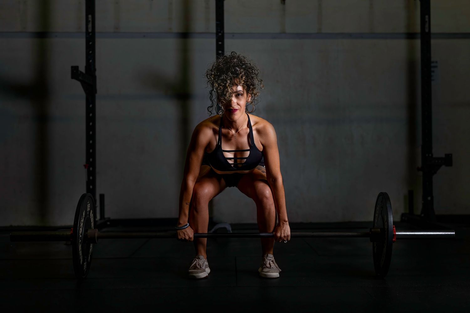 Person performing a weightlifting exercise with a barbell in a dark gym setting.