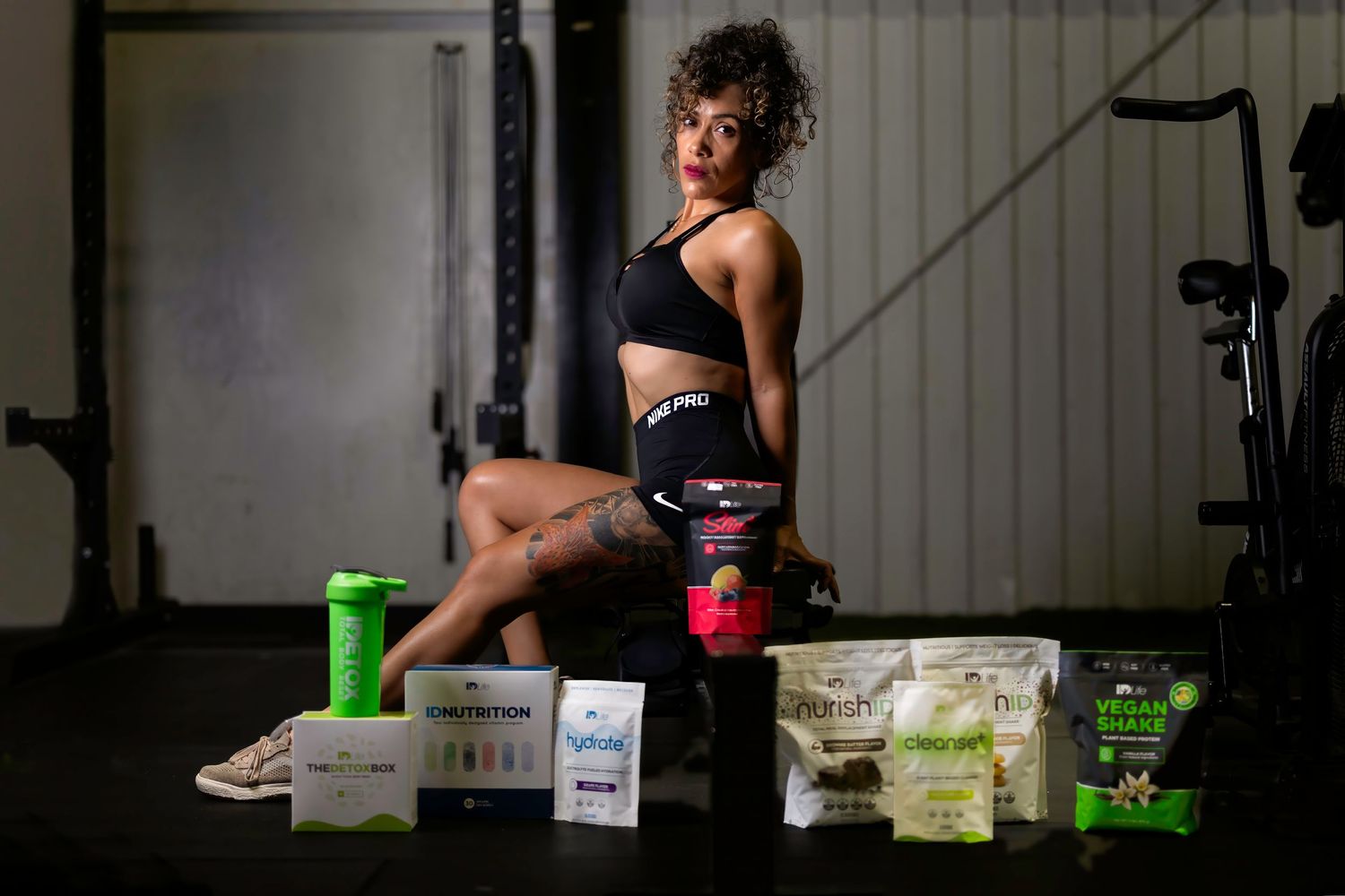 Fitness model posing with nutrition products in a dimly lit gym environment.