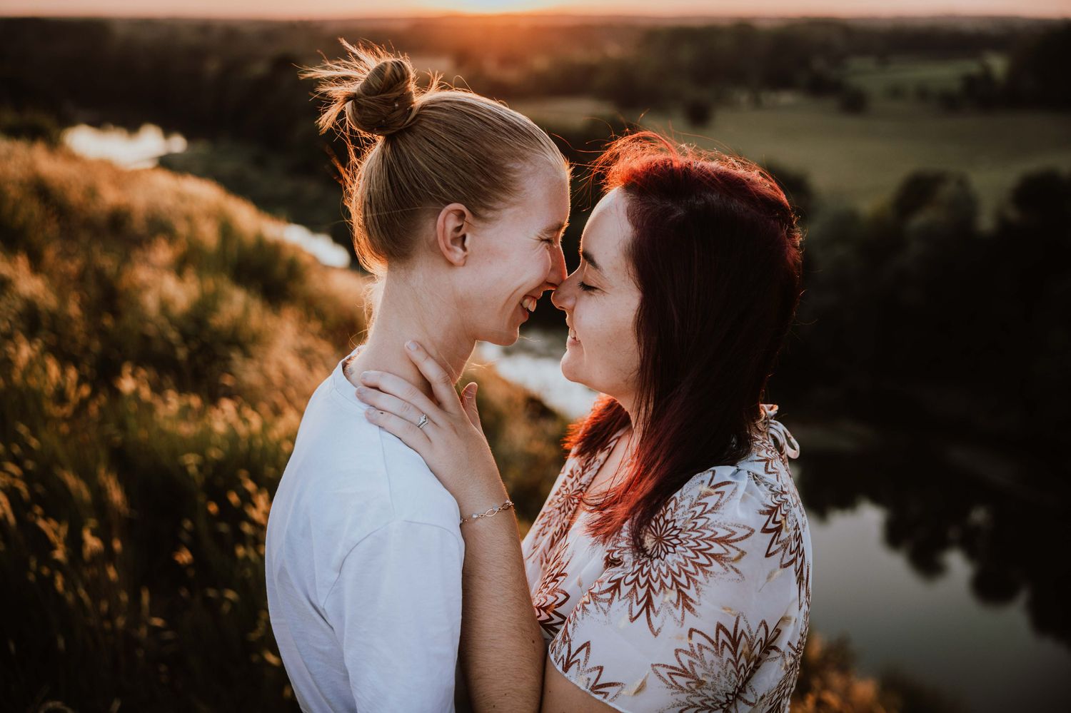 Couple embraces during golden hour sunset photoshoot by tranquil lake.