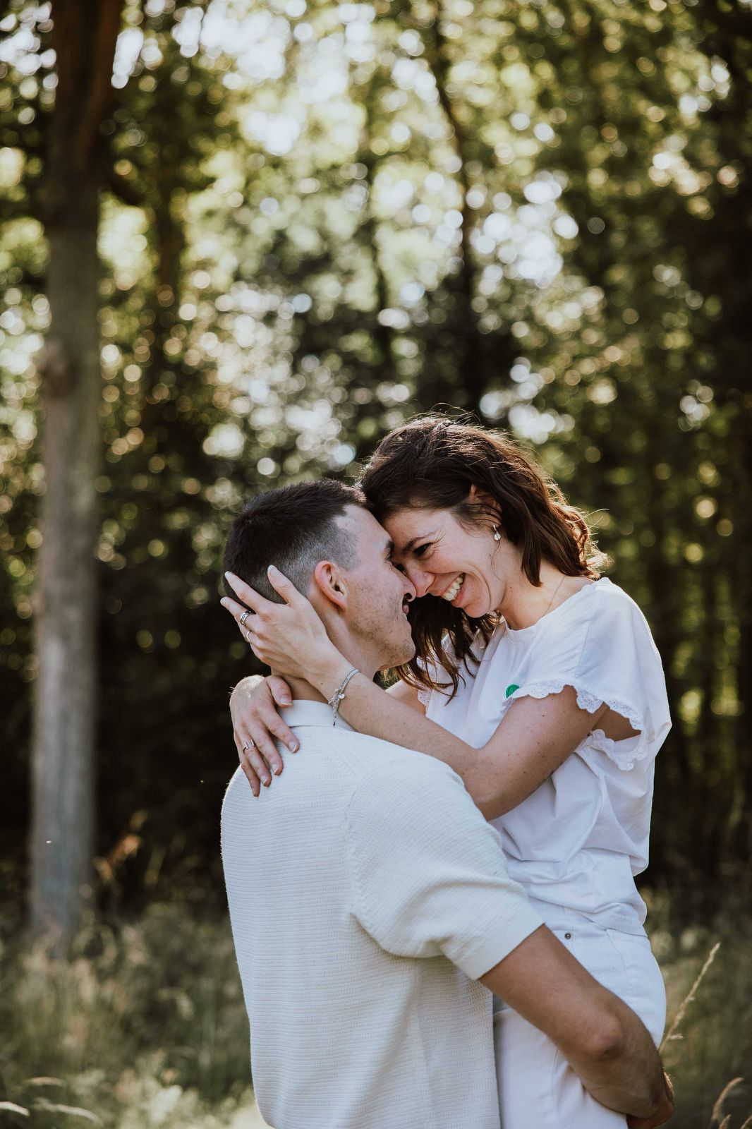 Couple in white outfits sharing intimate moments in a sun-dappled forest setting.