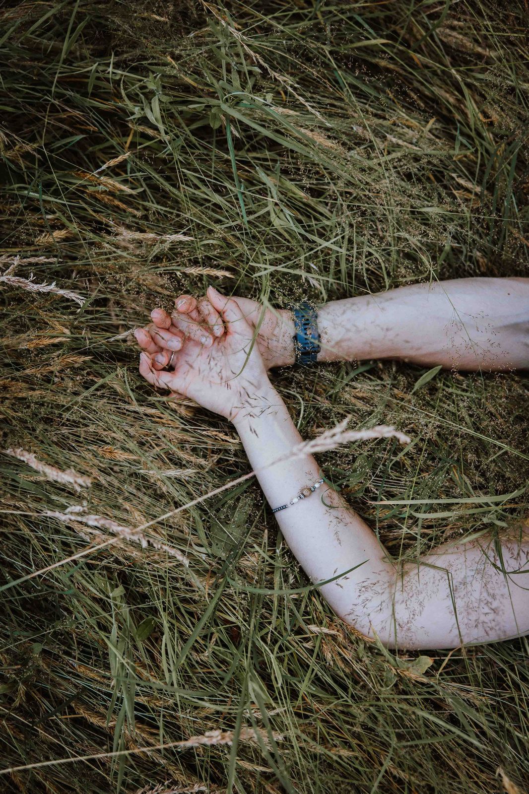 Two pale arms with delicate tattoos lying crossed on dry grass and hay.