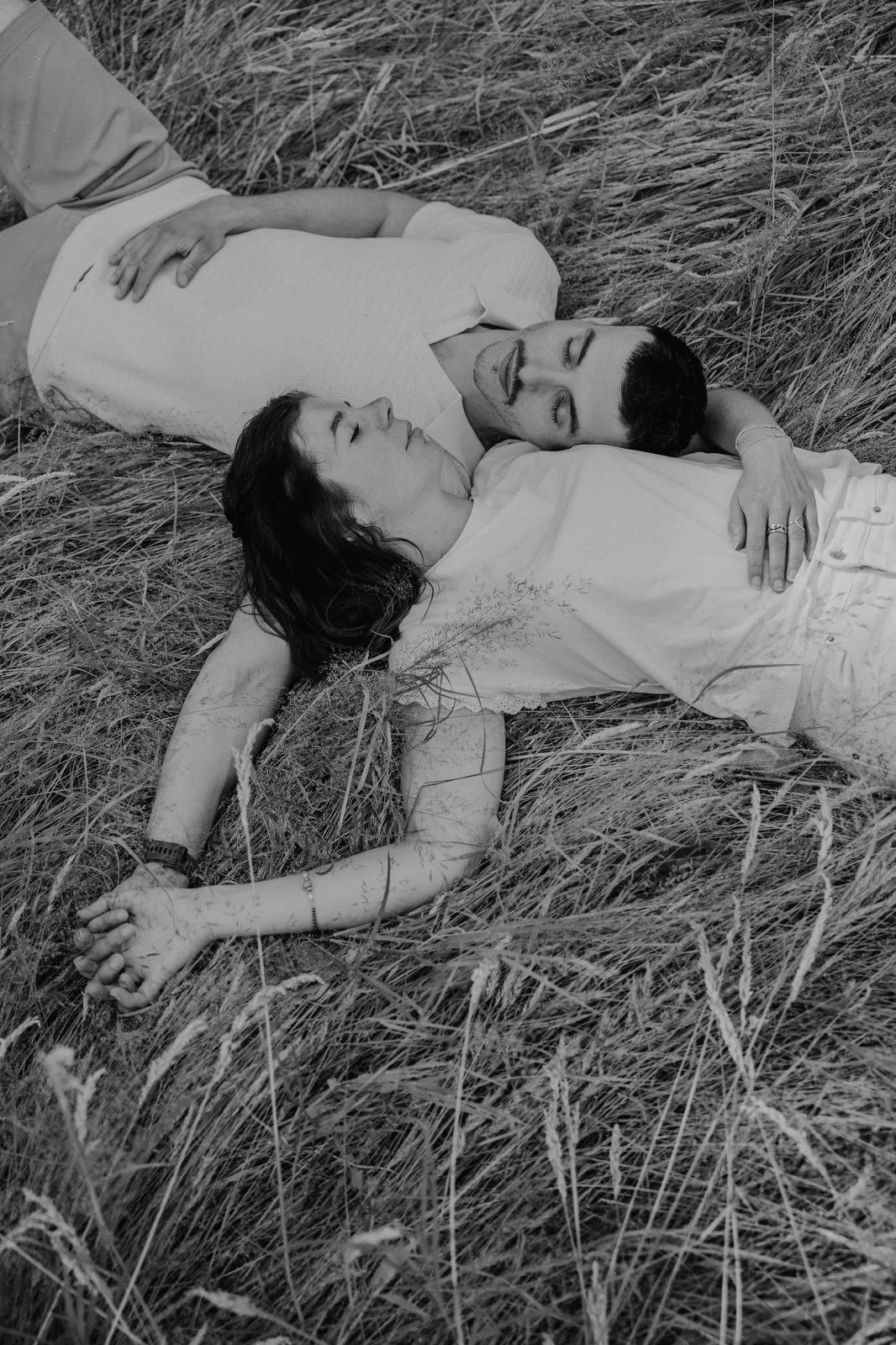 A person lies peacefully in tall grass wearing a white dress in this artistic black and white photo series.