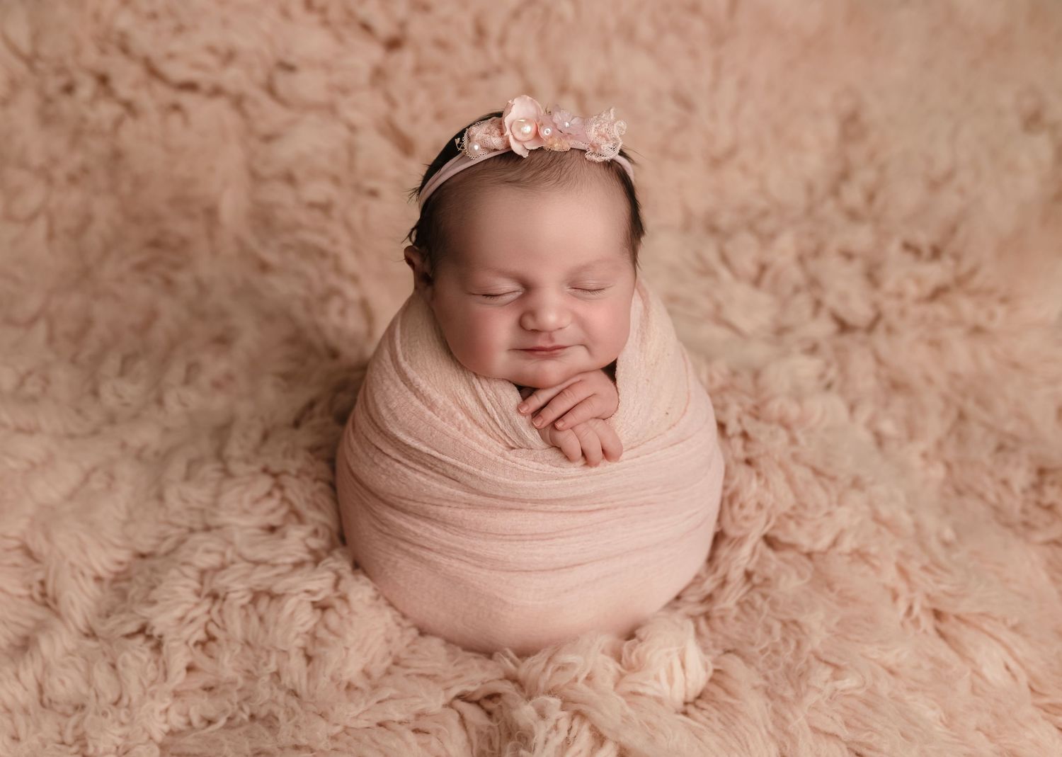 Baby girl wrapped in pink against a pink fur backdrop smiles, captured by Charlottesville newborn, maternity, and family photographer.