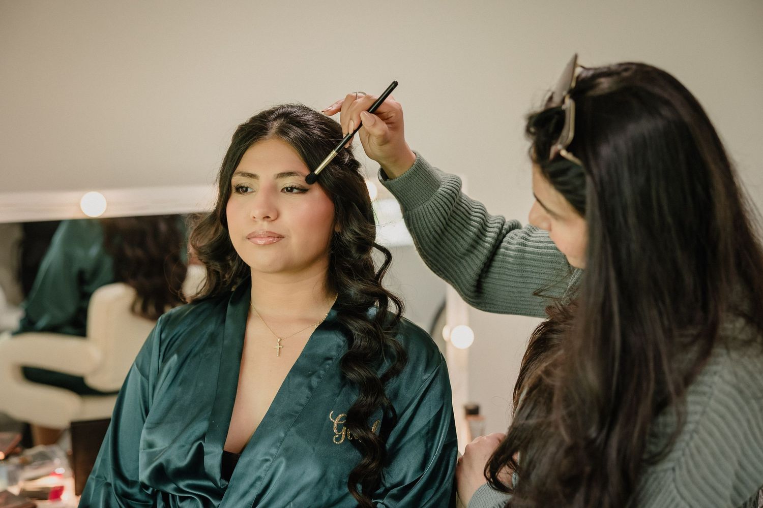 Professional makeup artist styles elegant curls while client wears emerald green silk robe during preparation session.