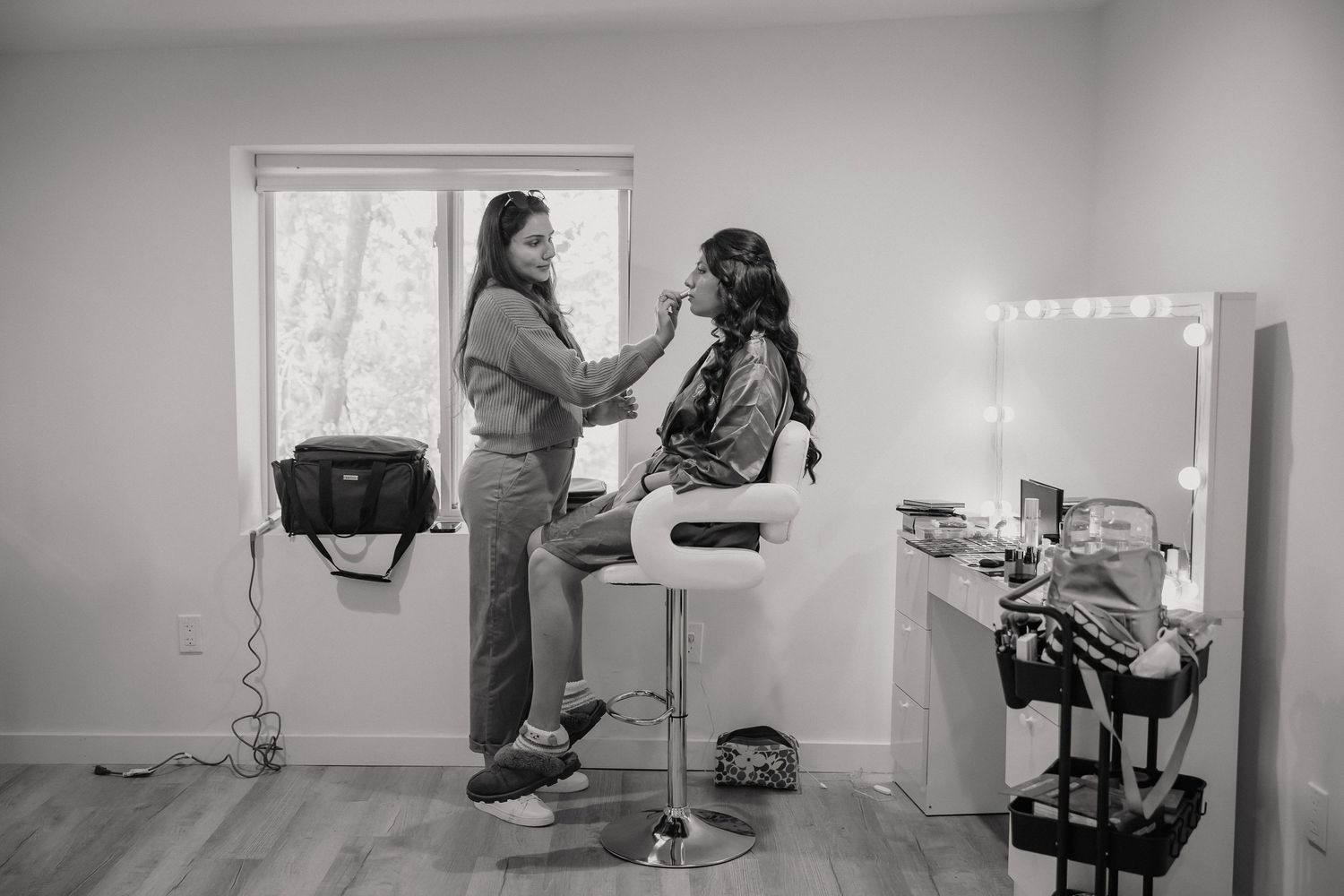 Black and white image of hairstyling session in modern makeup studio with vanity mirror.