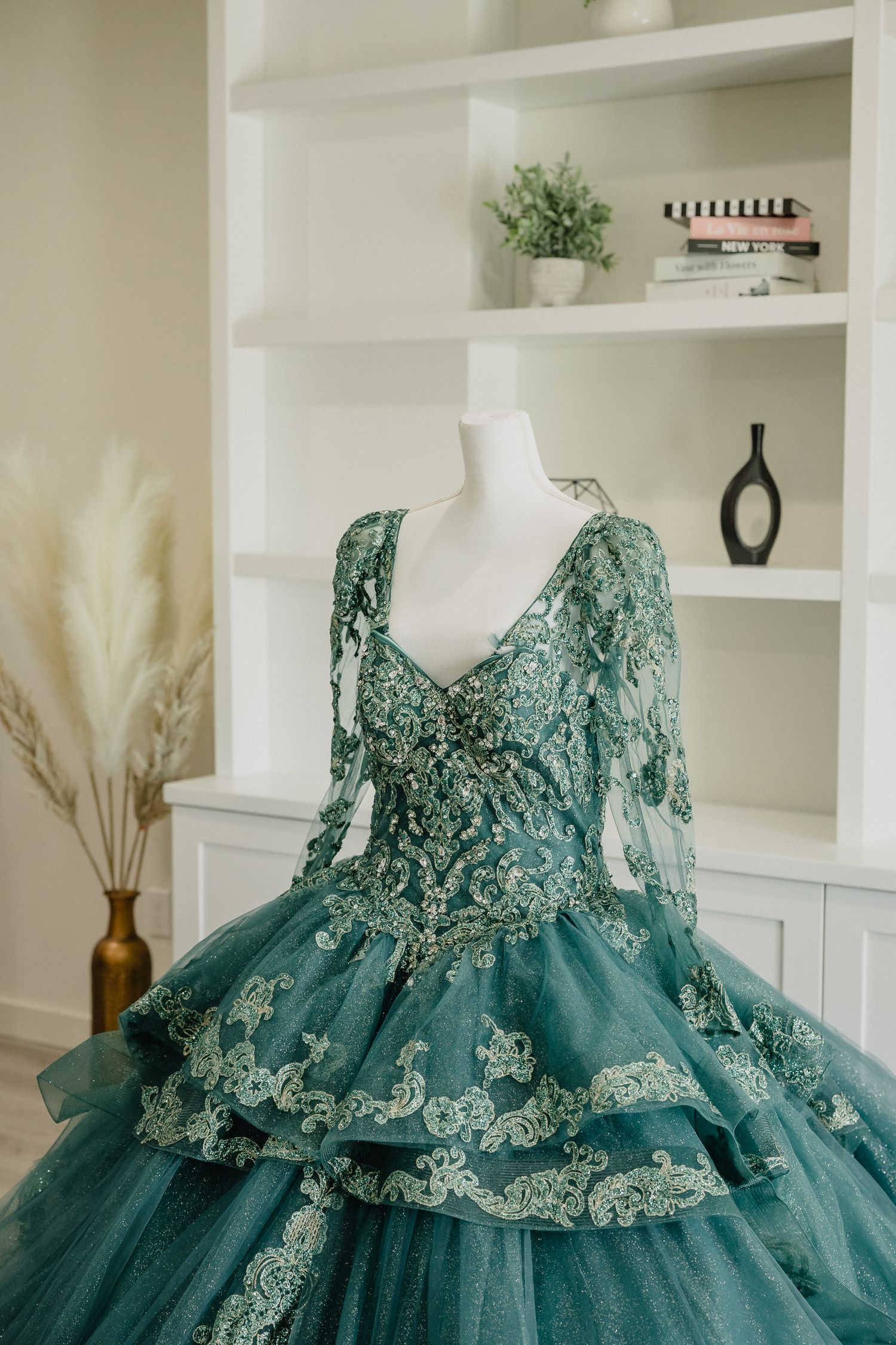 A teal green ball gown with intricate lace details and beading displayed on a mannequin form.