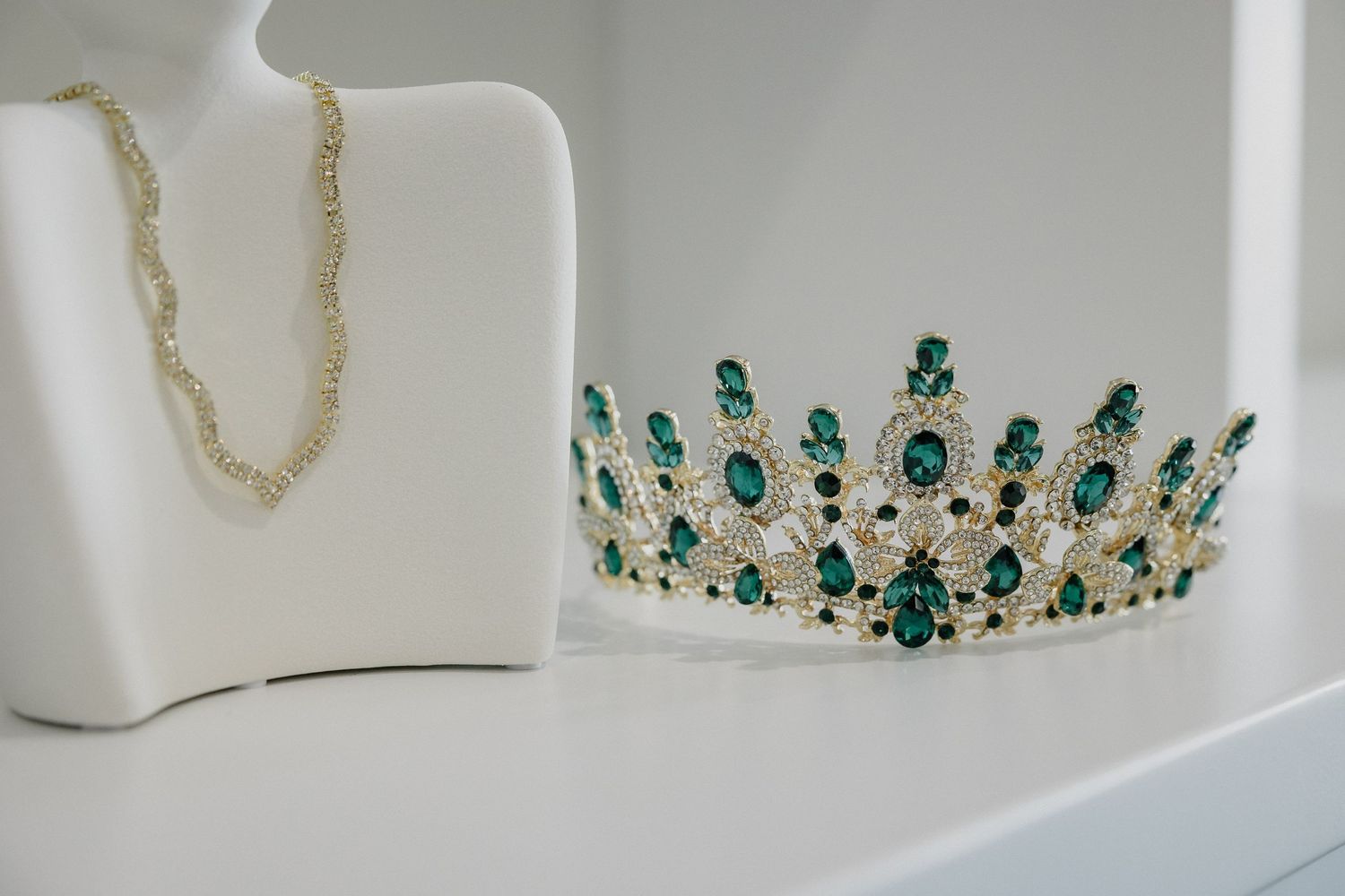An elegant silver and emerald green crystal tiara displayed next to a delicate necklace.