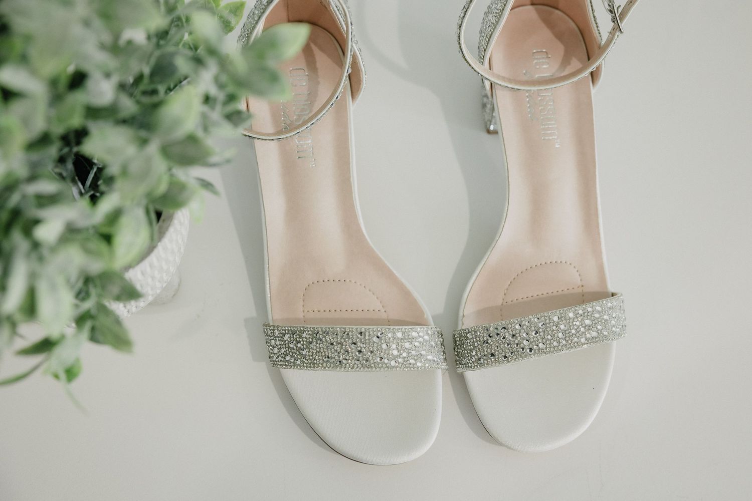 White rhinestone-embellished bridal sandals photographed with greenery.