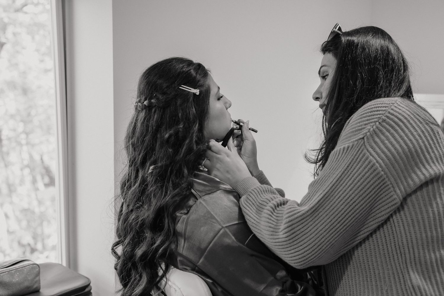 A behind-the-scenes moment of professional makeup application being done near a window.