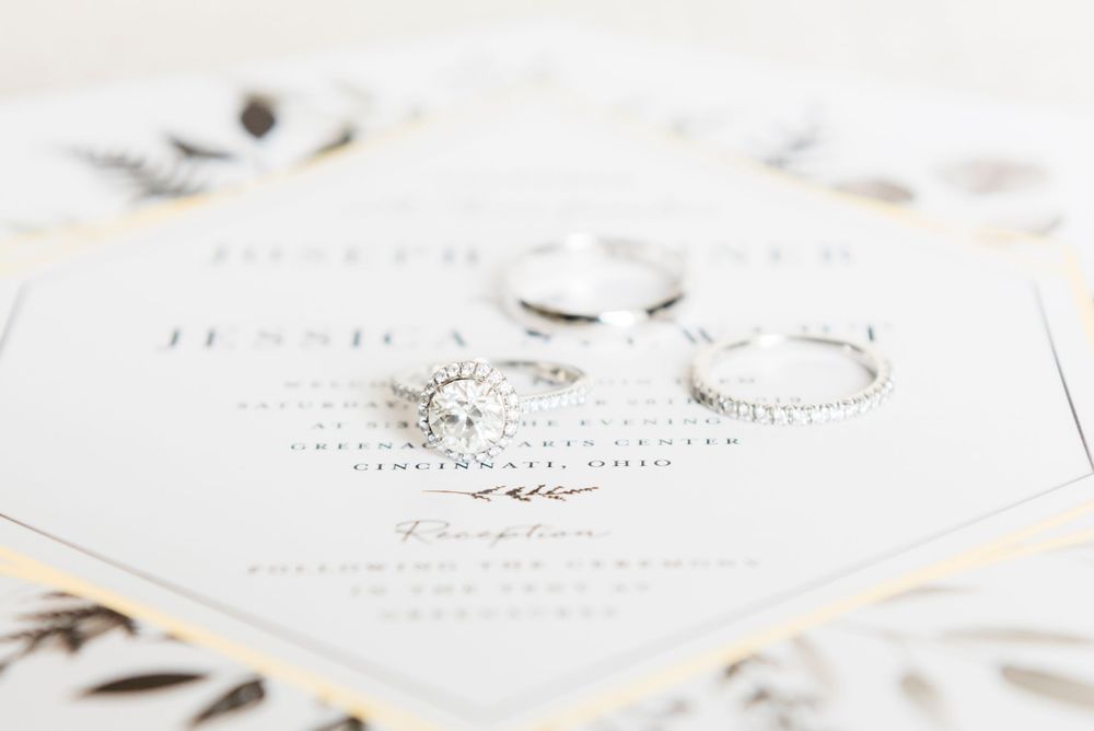 Wedding rings photographed on white invitation with delicate calligraphy details.