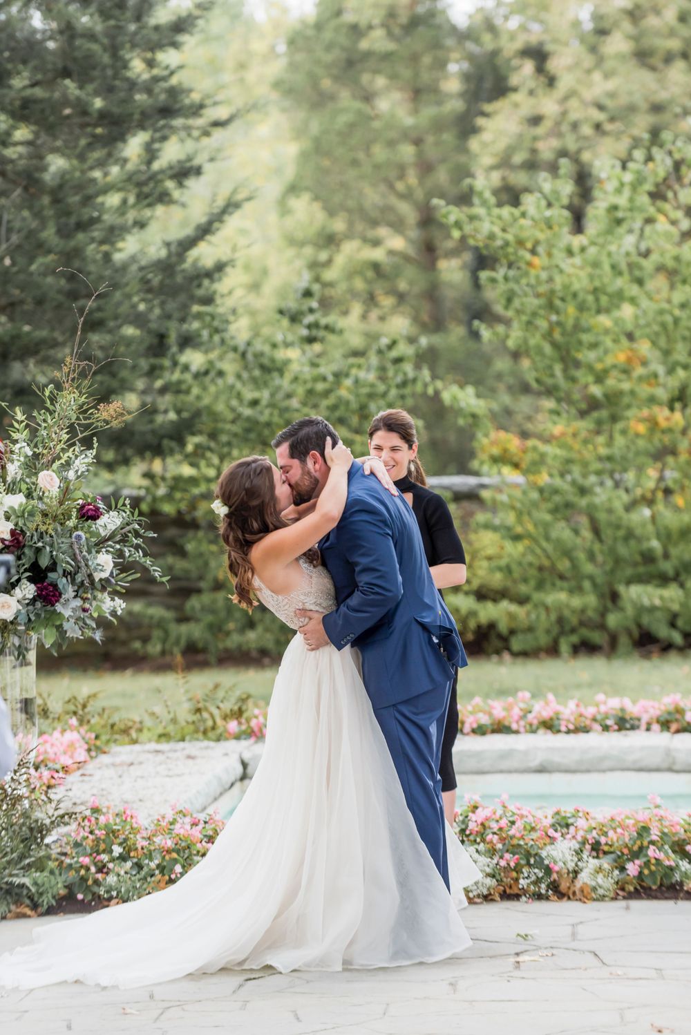 A romantic wedding moment in a garden setting with floral arrangements and elegant attire.