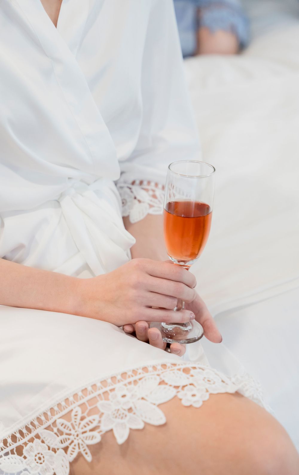 Close-up of lace wedding robe detail and champagne glass held by manicured hands.