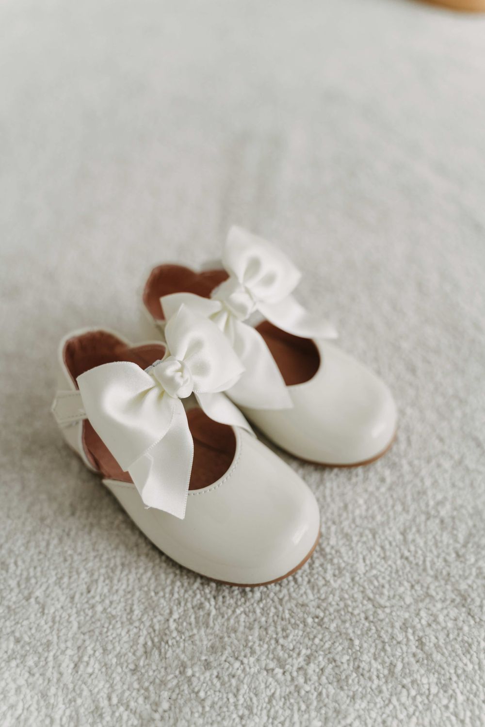 White baby shoes with bows on grey carpet.