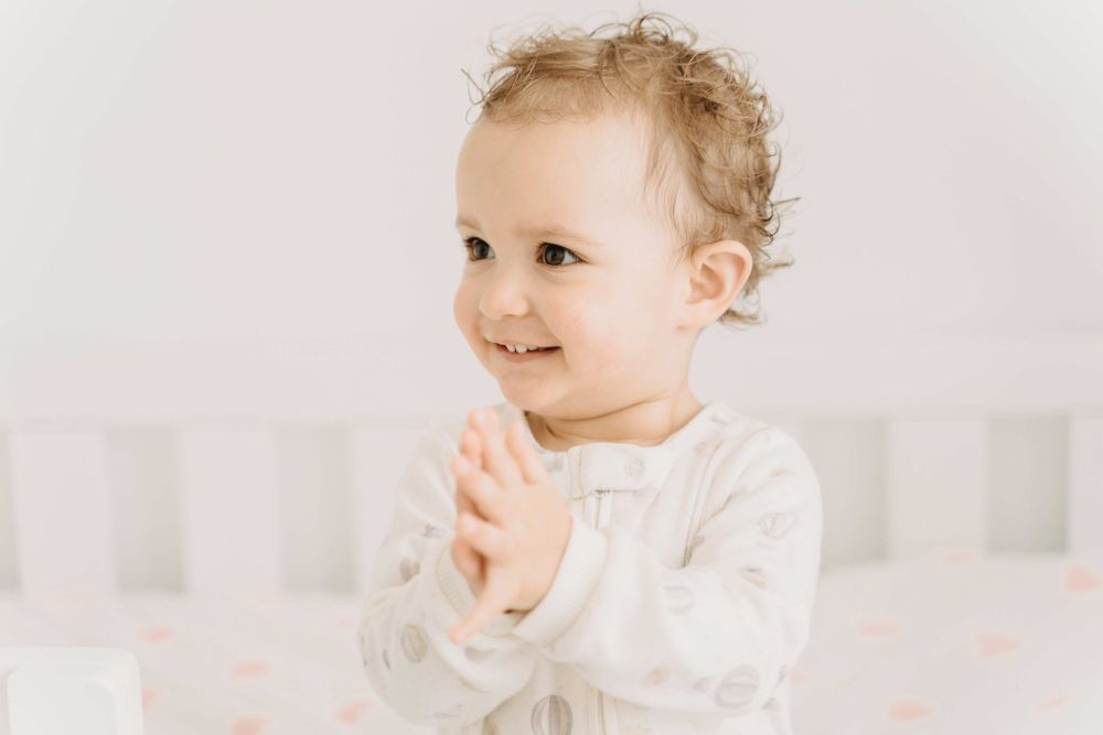Toddler in white outfit smiling and clapping hands.