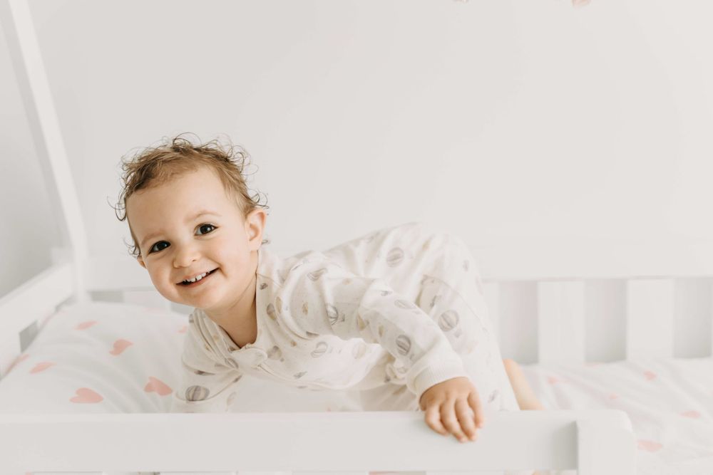 Smiling toddler in white pajamas lying on floral bedding.