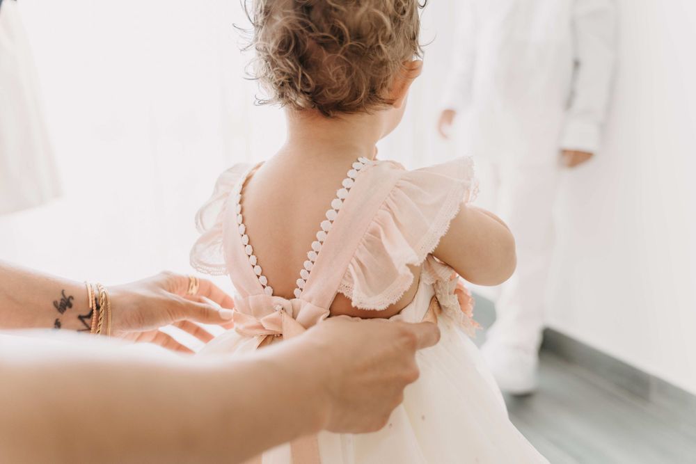 Hands fastening pearl buttons on pink ruffled dress from behind.
