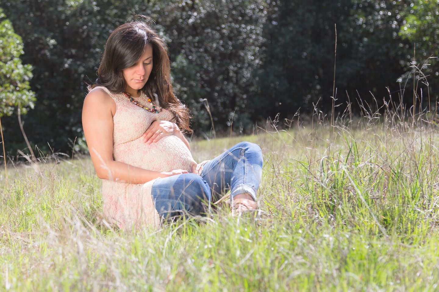 Mother maternity shot in the outdoors with the woman sitting Indian style in a field of grass. Eternity Fine Portraits