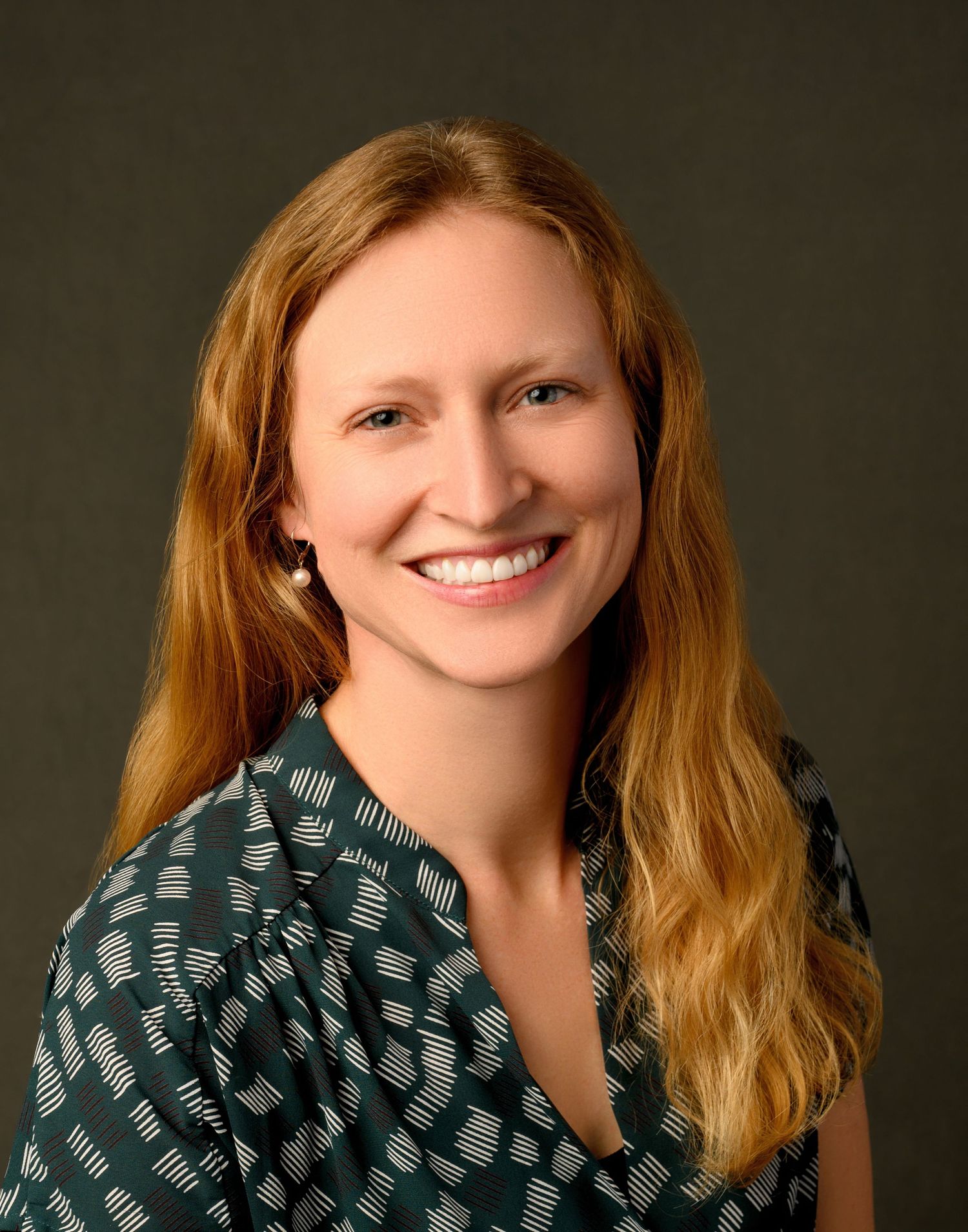 Professional studio portrait with warm lighting featuring person in patterned green top.