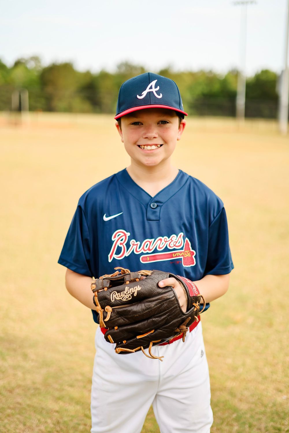 Young baseball player in Atlanta Braves uniform poses with glove on sunny field.