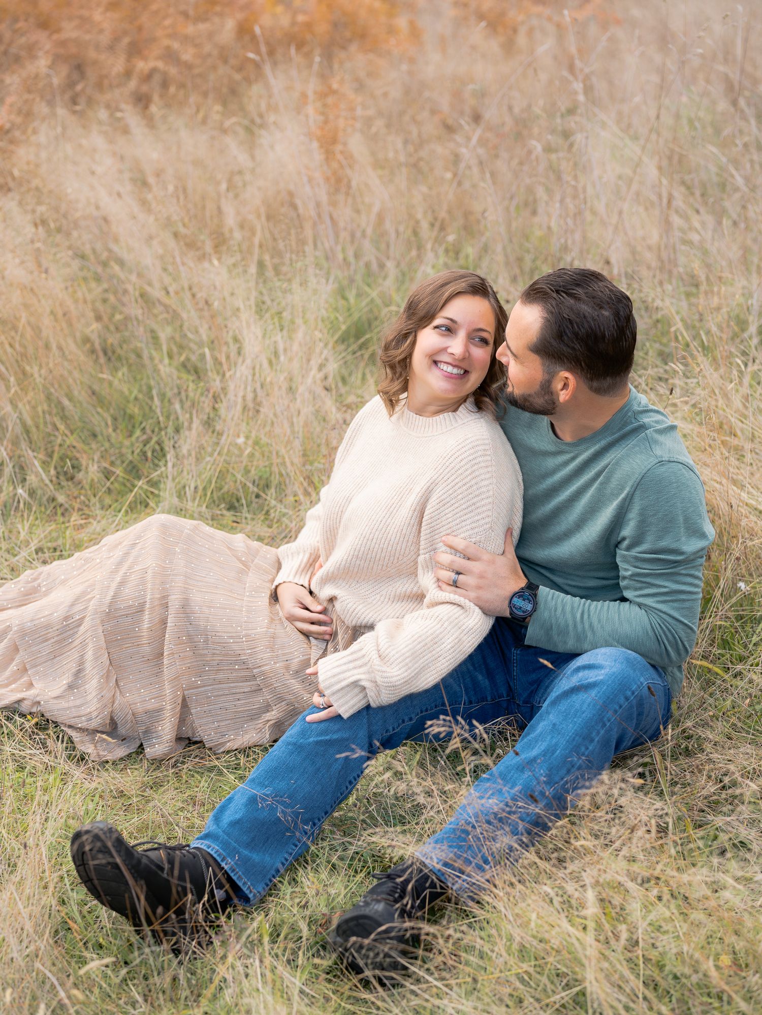 Couple sitting in golden grass field, leaning in for a kiss.