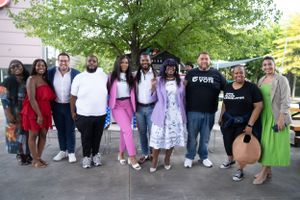 Group photo of diverse people standing together outdoors under tree.